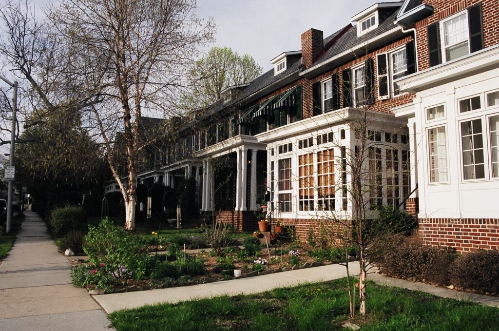 Brick rowhouses with large porches. Some have sunrooms. Landscaped gardens in front with blooming flowers.