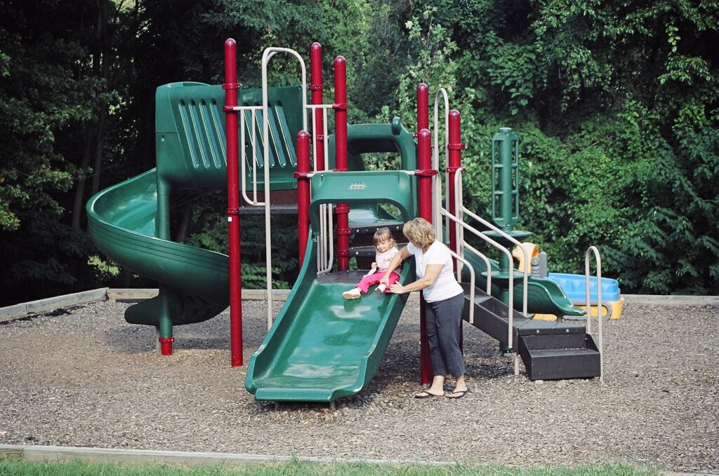 A mother helps her young daughter slide down the slide at the children's play area.