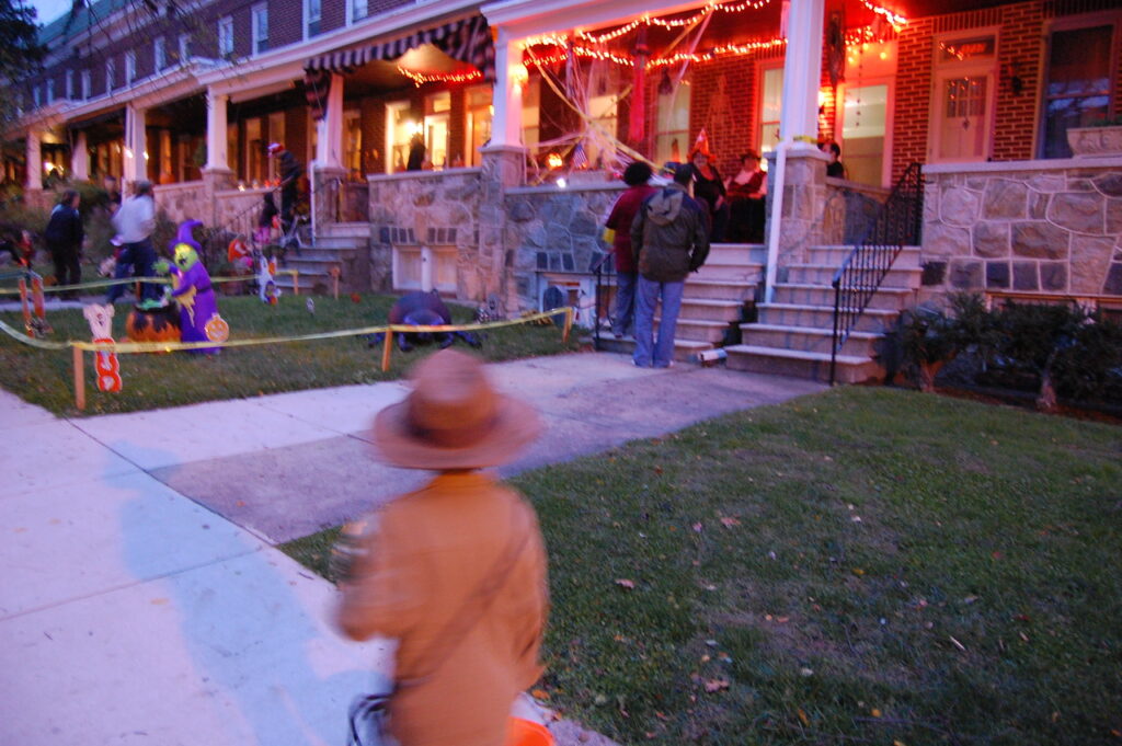 Halloween: a young trick or treater walks along a row of decorated houses.