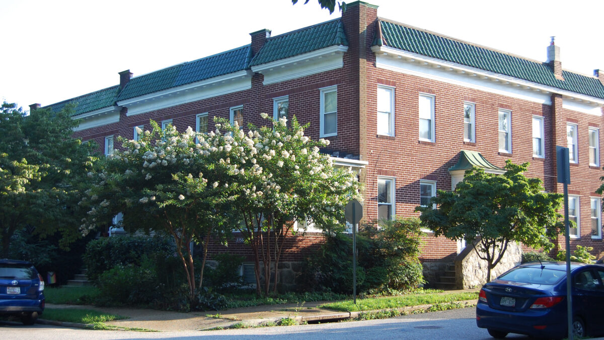 Corner view of a brick rowhouse with crepe myrtles blooming in front.