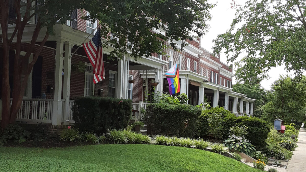 porches of row houses with hanging plants and flags. There are many trees and bushes.