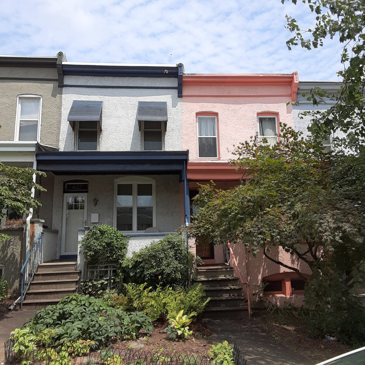 Stucco rowhouses painted different colors with leafy gardens in front.