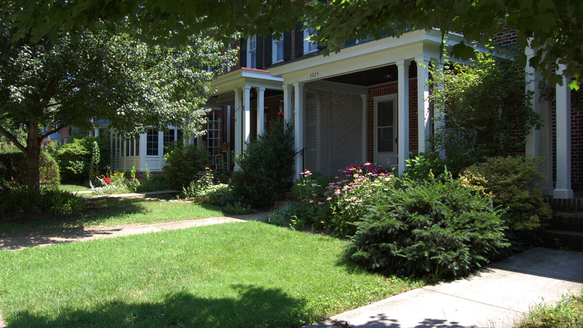 Green lawns lead up to covered porches. Flower gardens are in front.